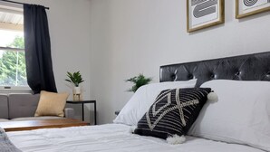 Een netjes ingerichte slaapkamer met een bed, een klein tafeltje, een sofa en een raam met gordijnen.