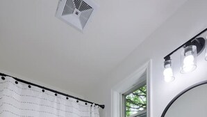 Een badkamer met een wit toilet, een witte wastafel met een ronde spiegel, en een douchegordijn met horizontale strepen.
