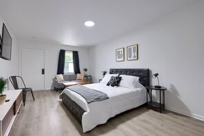 Quarto moderno com cama grande, escrivaninha, cadeira e janela com cortinas.