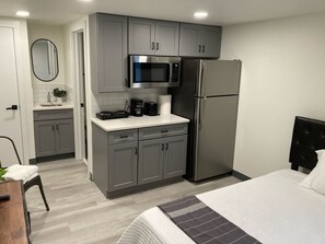 Une chambre d’hôtel de taille réduite, équipée d’une kitchenette, d’un lit et d’une chaise.