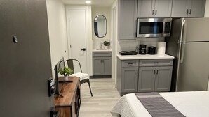 A compact hotel room with a bed, a desk with a chair, a microwave, a refrigerator, and a small kitchenette. - Boutique Motel in Strasburg (Ronks)