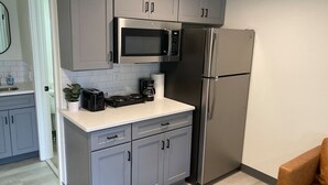 Eine moderne Küche mit grauen Schränken, einem Edelstahl-Kühlschrank, einer Mikrowelle und einer Kaffeemaschine auf der Arbeitsplatte.