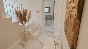 Un interior moderno con una escalera de mármol, un jarrón con plumas de miscania y un aplique de pared.