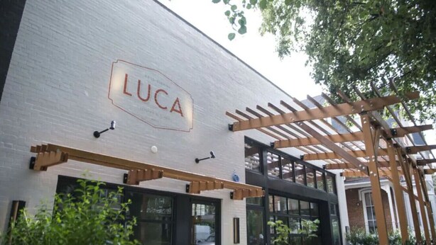 En modern byggnad med en skylt som visar ordet ”Luca” ovanför en glasdörr.