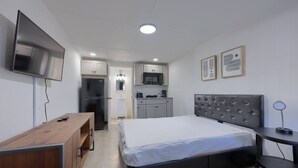 Ett kompakt hotellrum med en säng, ett skrivbord, en TV, ett litet kök och ett badrum.