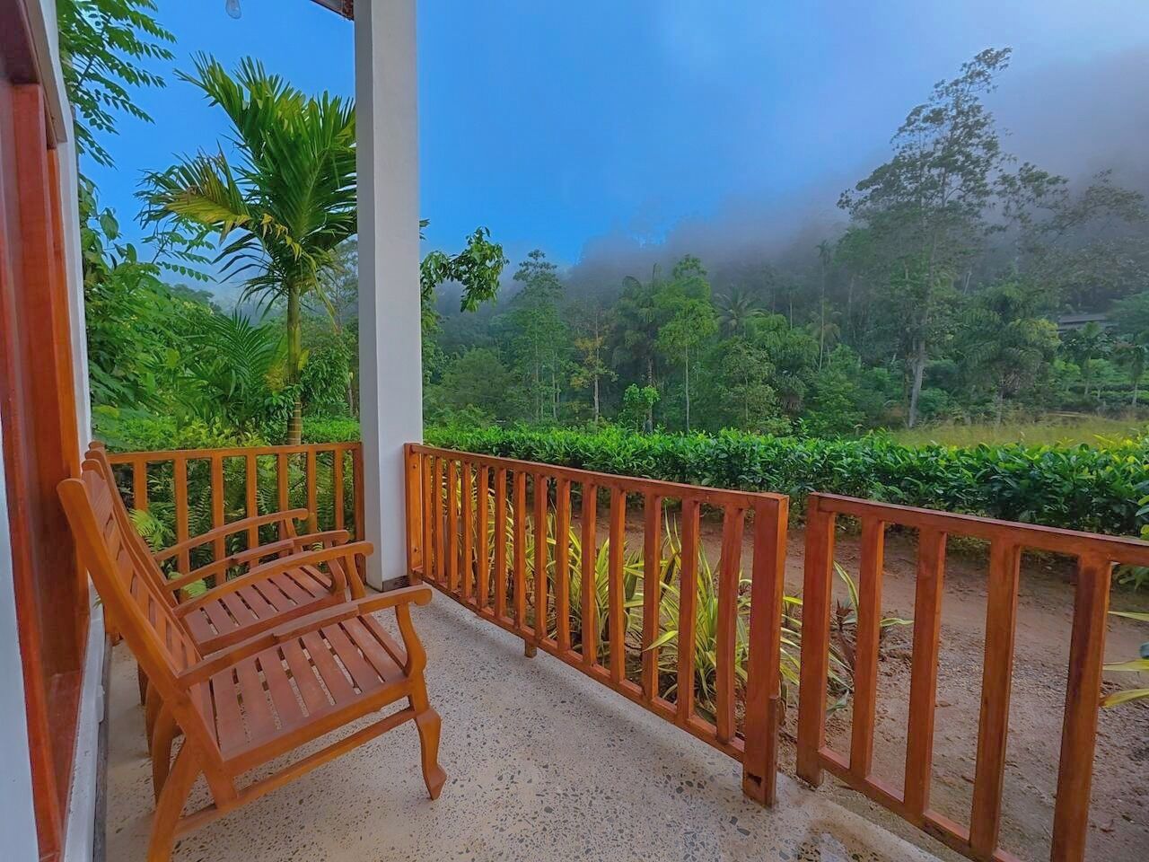 A wooden bench on a balcony with a view of a lush green landscape and trees.