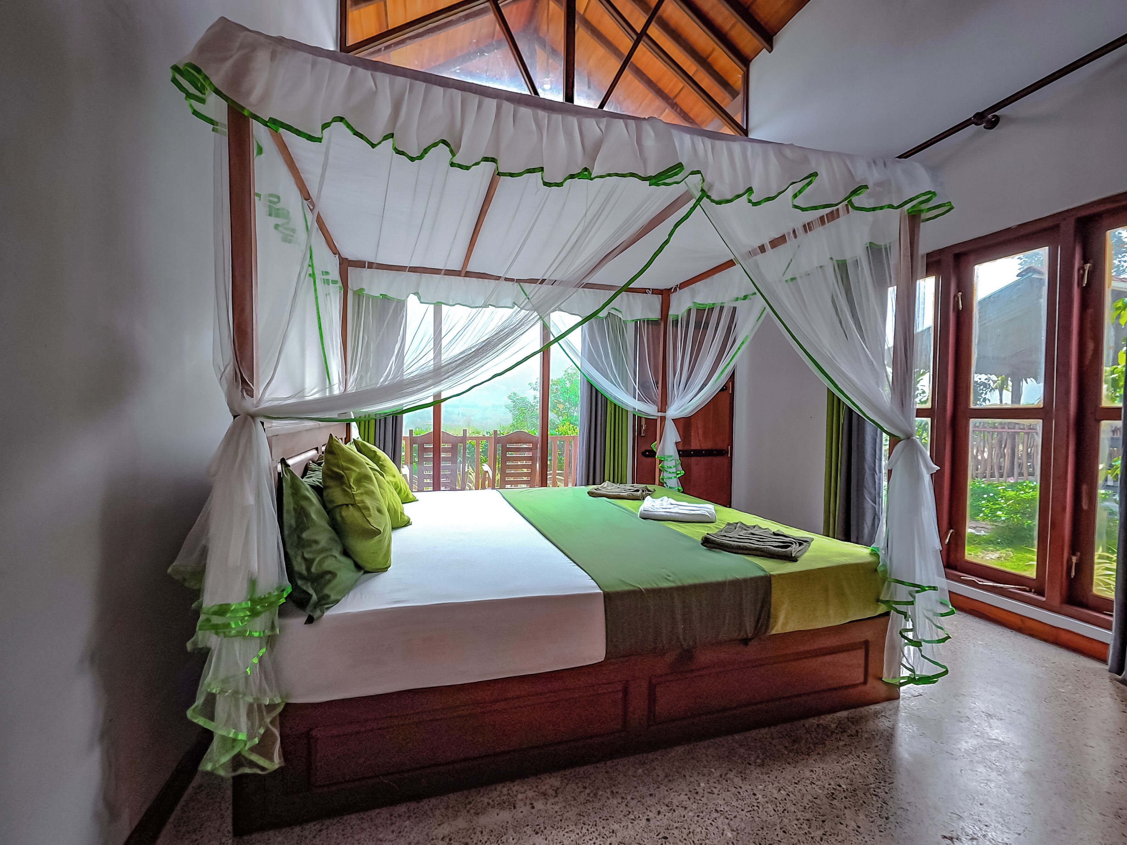 A four-poster canopy bed with a green bedspread, pillows, and a neatly made bed.