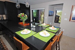 Eine moderne Küche mit einer großen Kochinsel, Esstisch mit grünen Platzsets und einer Blumenvase.