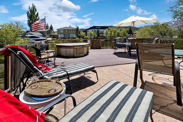 An outdoor patio with lounge chairs, a hot tub, and a wooden deck overlooking a body of water. - 1673 Venice Drive 4 Bedroom Home (South Lake Tahoe)
