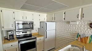 Uma cozinha com armários brancos, micro-ondas, frigorífico, forno, pia e máquina de café.