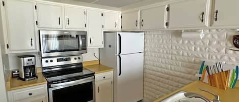 A kitchen with white cabinets, a microwave, a refrigerator, an oven, a sink, and a coffee maker.