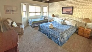 Quarto com duas camas, uma cadeira, uma escrivaninha e uma janela.