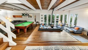 Un amplio salón con mesa de billar, chimenea y grandes ventanales con vistas al exterior.
