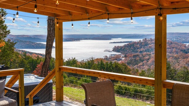 Una terraza de madera con un jacuzzi, sillas y vistas a un lago rodeado de árboles.