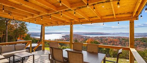 Una terraza de madera con mesa y sillas, con vistas a un paisaje pintoresco de un lago y un bosque.