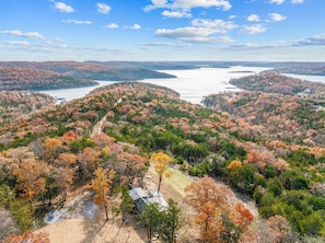 Vista panorámica de una zona montañosa con follaje otoñal, un lago y una cabaña pequeña.