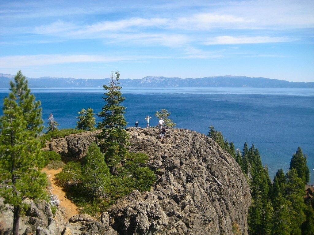 A rocky mountain peak with a clear view of a large body of water and distant mountains.