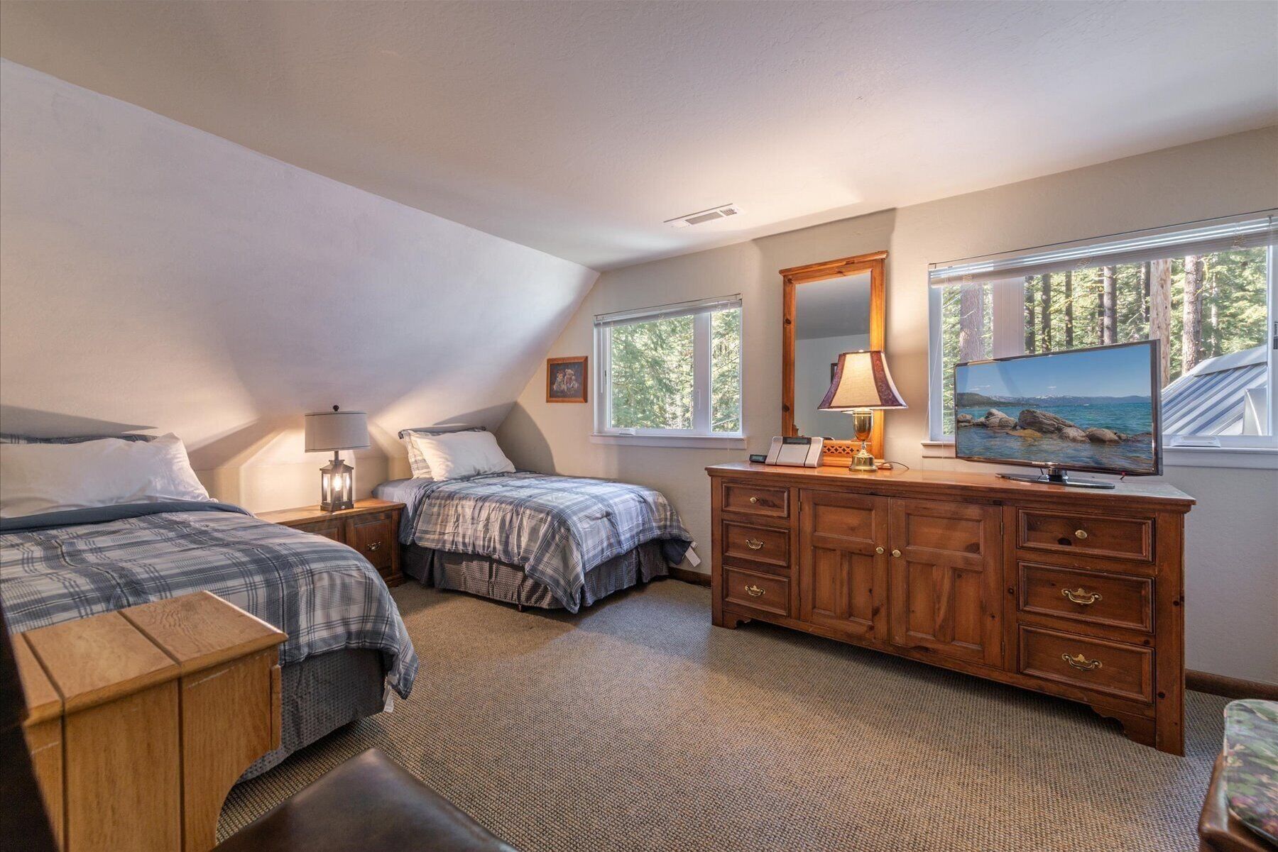 A bedroom with two beds, a dresser, a TV, and a window with a view of trees.