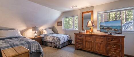 A bedroom with two beds, a dresser, a TV, and a window with a view of trees.