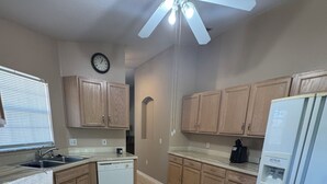 A kitchen with wooden cabinets, a white refrigerator, a stove, and a ceiling fan. - Welcome to resort style living in Kissimmee! (Kissimmee)