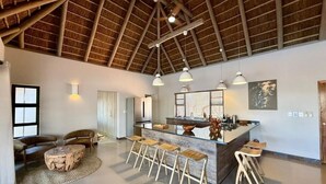 A spacious living area with a high ceiling, a central island with stools, a sofa, and a coffee table. - Luxury Bush villa for rent in Hoedspruit, near Kruger National Park (Hoedspruit)