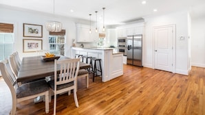 A modern kitchen with white cabinetry, a wooden dining table, and a central island. - 6 Bedroom IOP Home w/ Community Pool Just Outside | Steps from Beach and Fun (Isle of Palms)