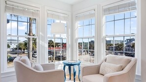A room with large windows, a blue table, and two beige armchairs. - 6 Bedroom IOP Home w/ Community Pool Just Outside | Steps from Beach and Fun (Isle of Palms)