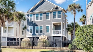 A two-story residential building with a grey exterior, white trim, and multiple windows. - 6 Bedroom IOP Home w/ Community Pool Just Outside | Steps from Beach and Fun (Isle of Palms)