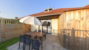 An outdoor patio area with a table and chairs, a wooden fence, and a covered seating area. - Grosszugige Ferienwohnung fur bis zu 9 Personen (Butjadingen)