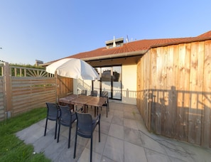 An outdoor patio area with a table and chairs, a wooden fence, and a covered seating area. - Grosszugige Ferienwohnung fur bis zu 9 Personen (Butjadingen)