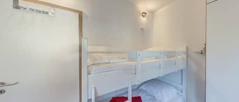 Un dormitorio con literas, una puerta, una lámpara y un estante pequeño.