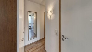 A hallway with a wooden floor, a white door with a silver handle, and a wall-mounted light fixture. - Grosszugige Ferienwohnung fur bis zu 9 Personen (Butjadingen)