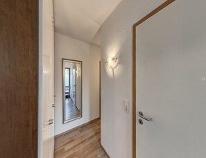 A hallway with a wooden floor, a white door with a silver handle, and a wall-mounted light fixture. - Grosszugige Ferienwohnung fur bis zu 9 Personen (Butjadingen)