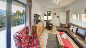 A spacious living room with a large window, a television, a sofa, a coffee table, and a fireplace. - Grosszugige Ferienwohnung fur bis zu 9 Personen (Butjadingen)
