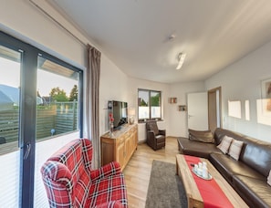 A spacious living room with a large window, a television, a sofa, a coffee table, and a fireplace. - Grosszugige Ferienwohnung fur bis zu 9 Personen (Butjadingen)