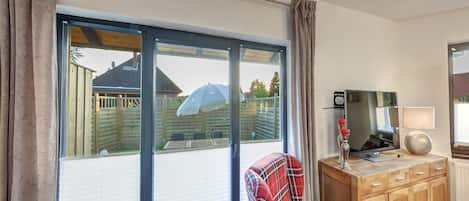 A room with a large sliding glass door, a plaid chair, a wooden cabinet, and a television.