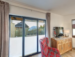 A room with a large sliding glass door, a plaid chair, a wooden cabinet, and a television. - Grosszugige Ferienwohnung fur bis zu 9 Personen (Butjadingen)
