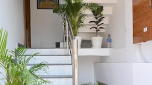 A modern staircase with white steps and a metal railing, flanked by potted plants. - Pitambara Homestay (Faizabad)