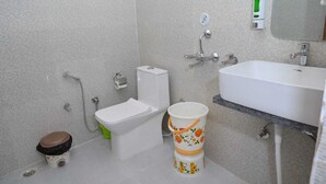 A bathroom with a toilet, bidet, sink, and a bucket. - Pitambara Homestay (Faizabad)