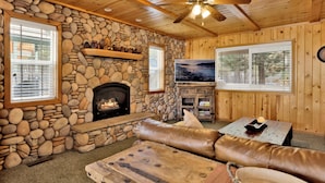 A cozy cabin interior with a stone fireplace, wooden ceiling, and a stone wall. - Brownie Resort Retreat | Walk-to-Ski Snow Summit Duplex Getaway (Big Bear Lake)