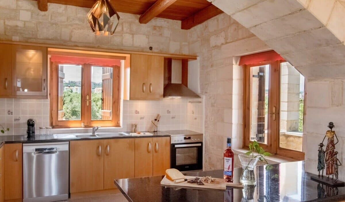 Eine Küche mit Holzschränken, einem eingebauten Backofen und einem großen Fenster mit Blick ins Grüne.