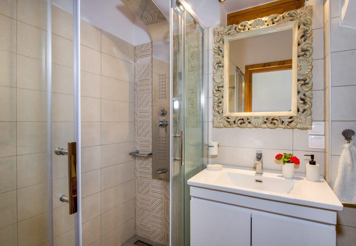 A bathroom with a glass shower enclosure, a white vanity with a mirror, and a decorative wall panel.