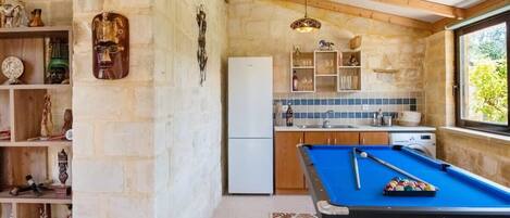 A cozy kitchen with a pool table, stone walls, wooden beams, and a window with a view.