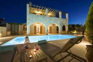 A swimming pool with lounge chairs and a table, a stone building with arched doorways, and a pergola structure. - Luxury stone villa with big private pool at beach (Tavronitis)
