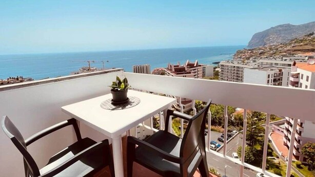 Un balcone con tavolo e due sedie, vista sulla città costiera e sul mare.