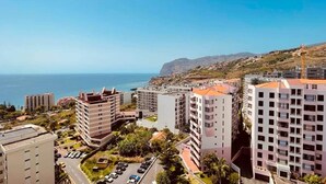 Una zona residenziale costiera con edifici a più piani, vista chiara sul mare e un paesaggio collinare sullo sfondo.