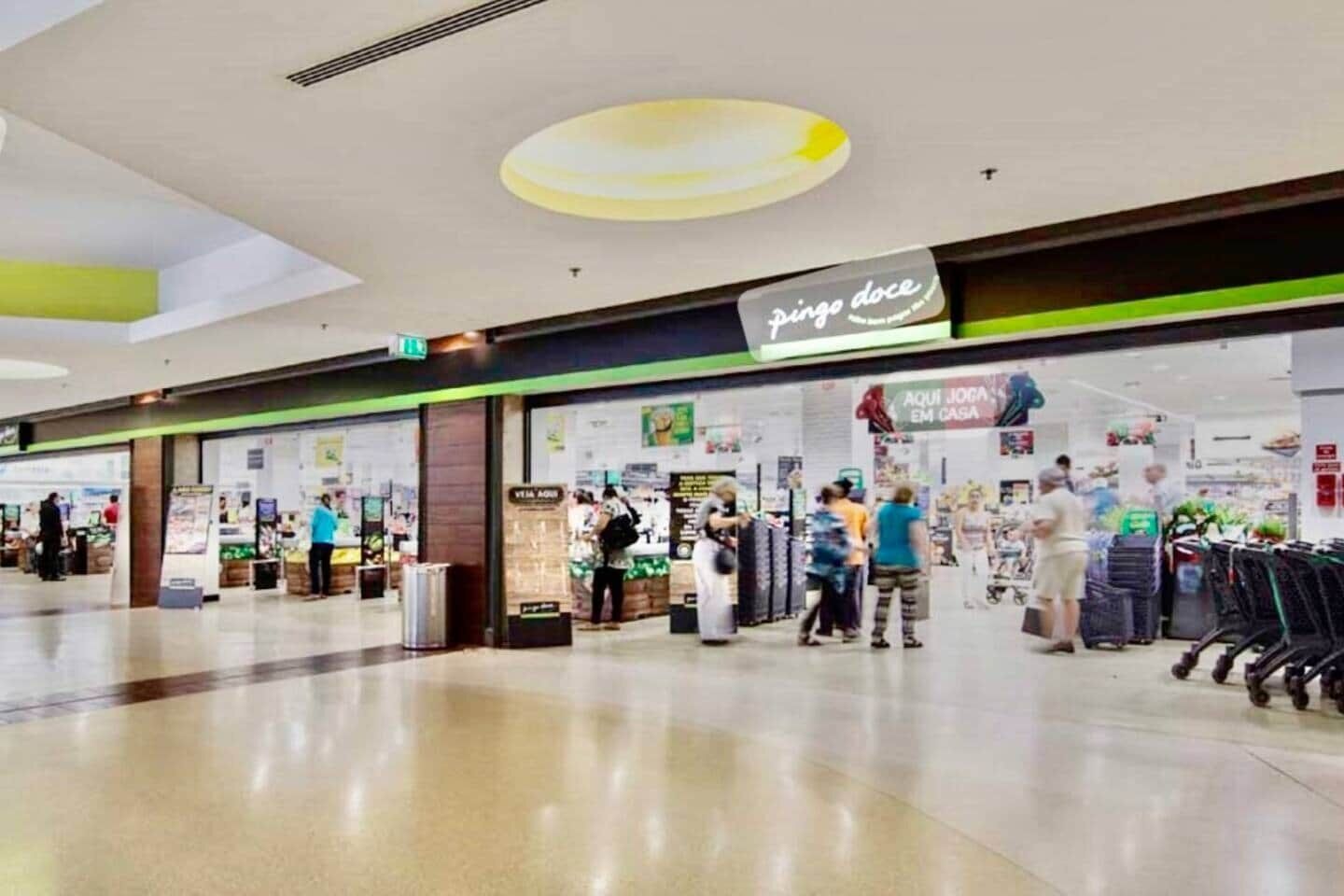 A shopping mall with a 'pingo doce' store, various kiosks, and shoppers.