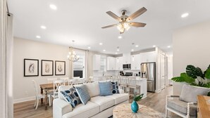 A spacious living area with a sofa, dining table, and chairs, a kitchen with white cabinets, and a ceiling fan. - Horizon Dreams | Duplex One Block from Beach w. Two Pools (Panama City Beach)