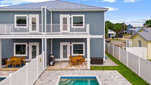 A two-story house with a balcony, a pool, and a patio area with outdoor furniture. - Horizon Dreams A | One Block from Beach, Private Pool, Fenced-In Yard (Panama City Beach)