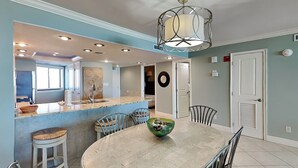 A modern kitchen with a central island, a dining table with chairs, and a ceiling light fixture. - Edgewater #611 | Beach Access, Pool, Gym, Hot Tub, Grills + More (Miramar Beach)